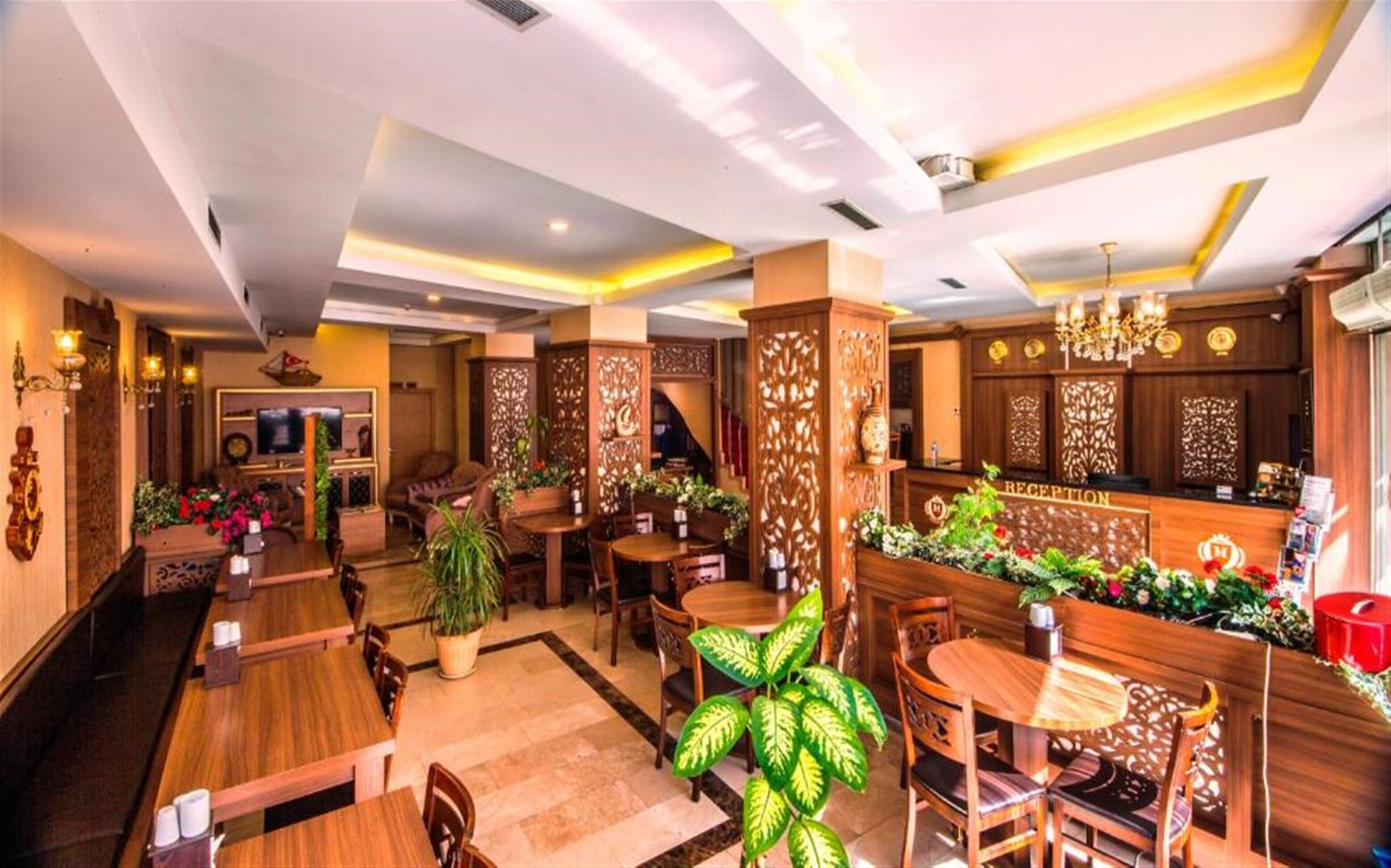 A hotel lobby with wooden furniture, a reception desk, and decorative plants.