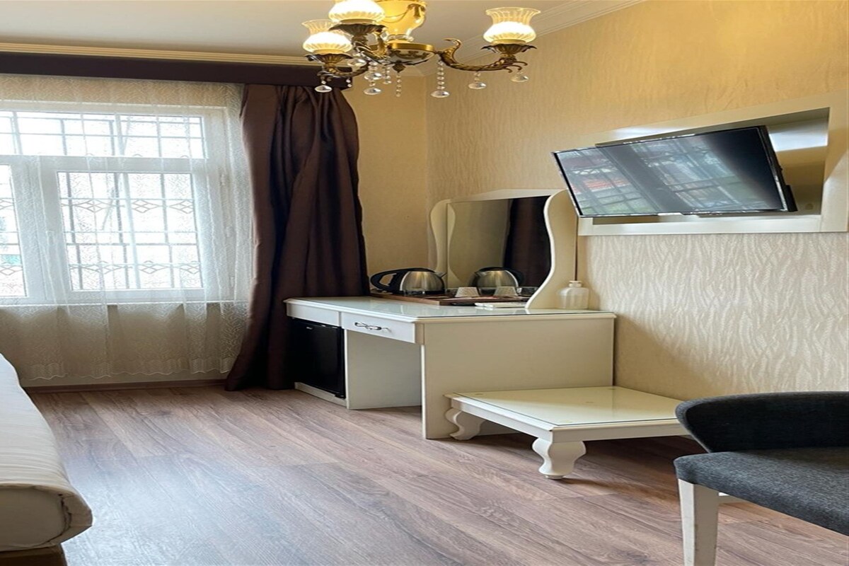 A hotel room with a desk, chair, television, and a window with curtains.