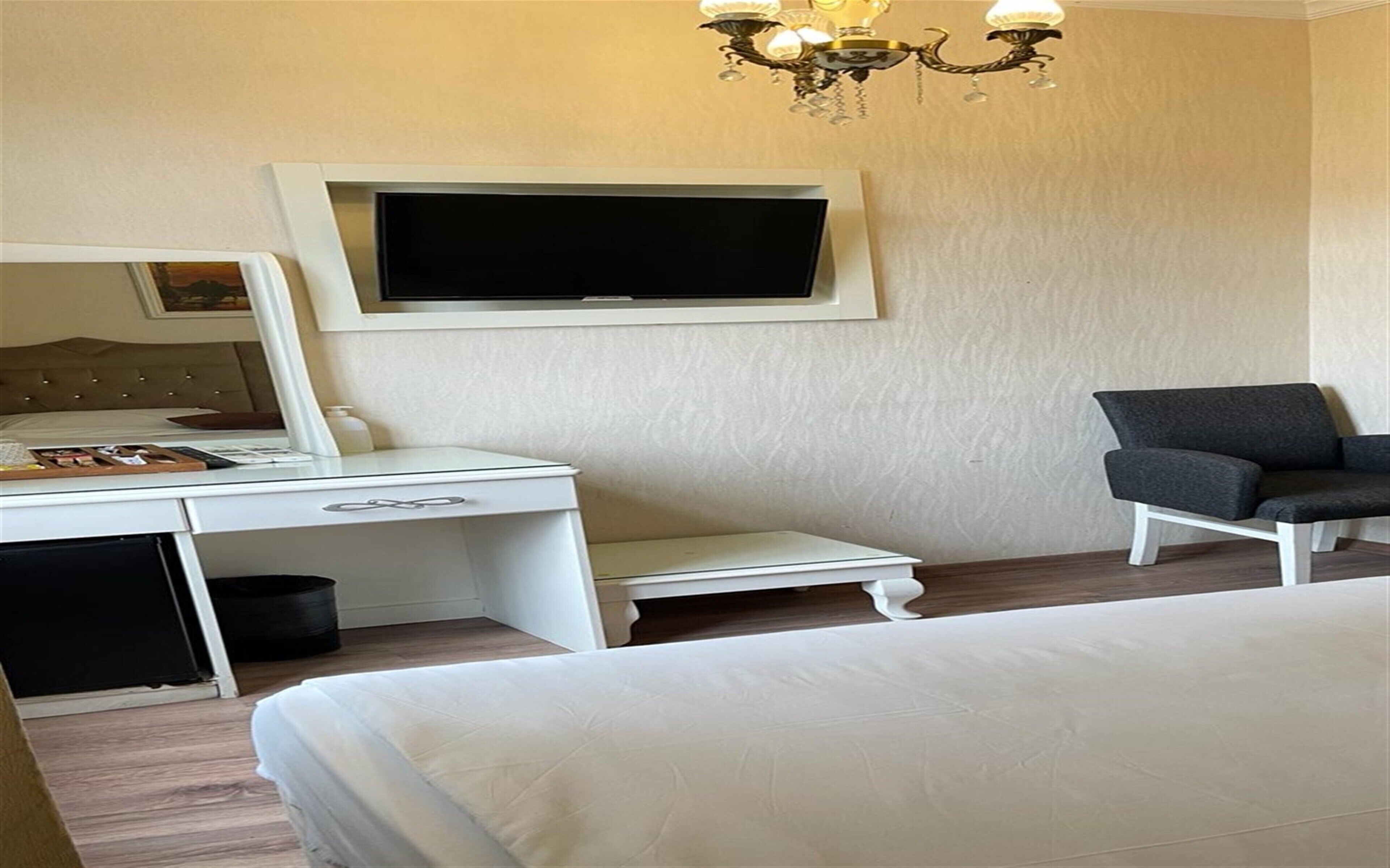 Een hotelkamer met een bed, een bureau met spiegel, een aan de muur bevestigde televisie en een kleine fauteuil.