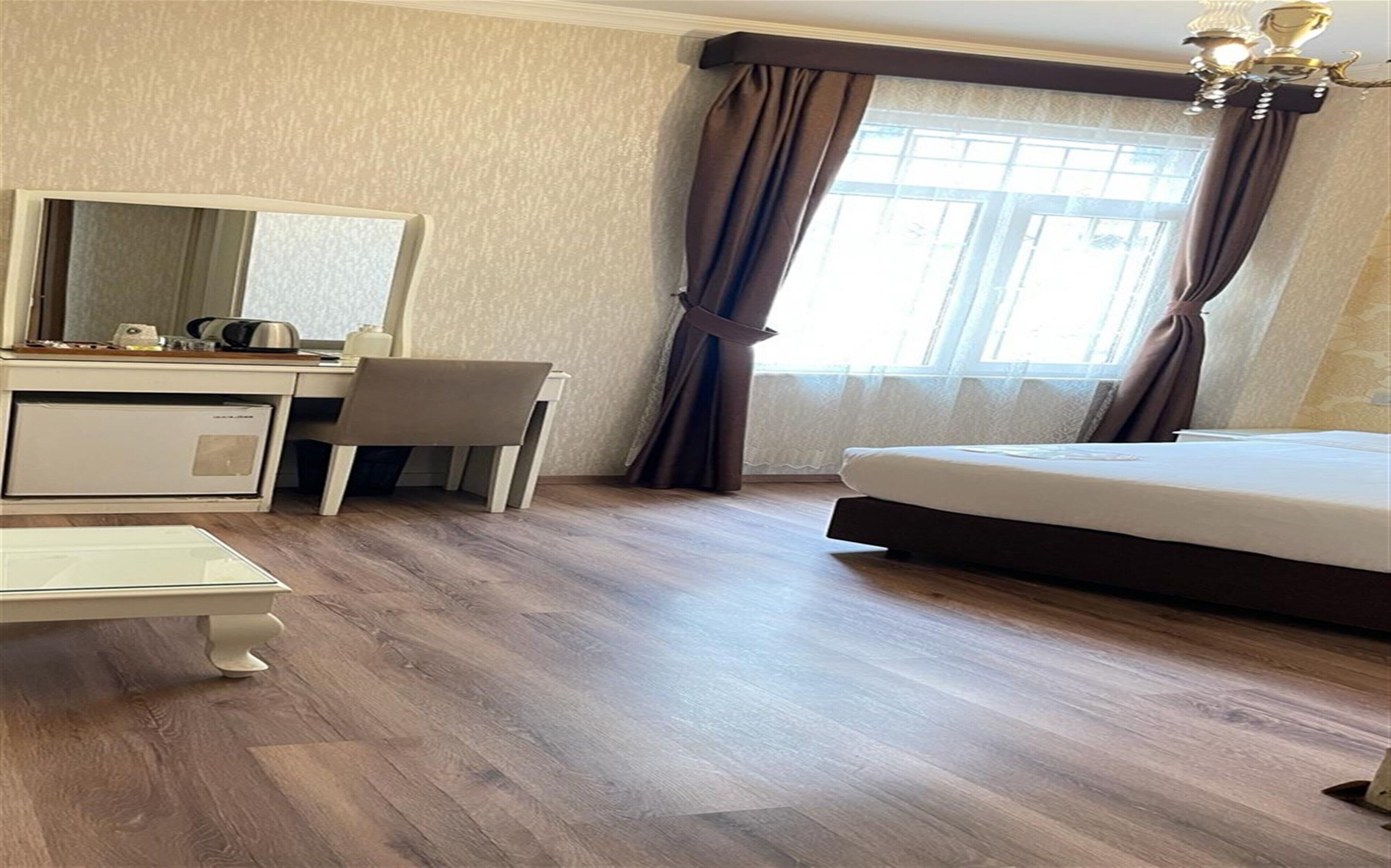 Una camera d'albergo con un letto, una scrivania con una sedia, un piccolo frigorifero e una finestra con tende.