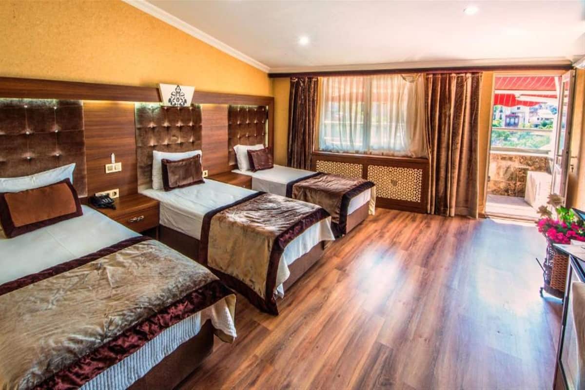 Habitación de hotel con tres camas, piso de madera y un ventanal con cortinas.