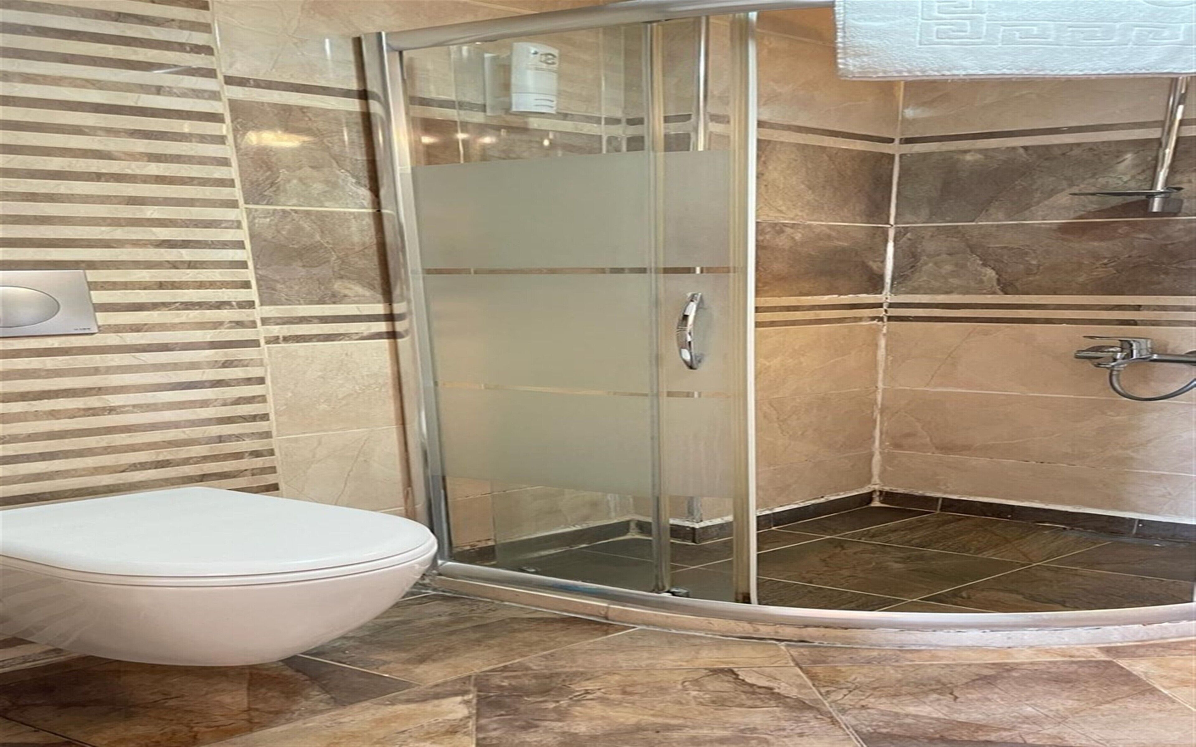 A bathroom with a glass-enclosed shower, a toilet, and tiled walls.