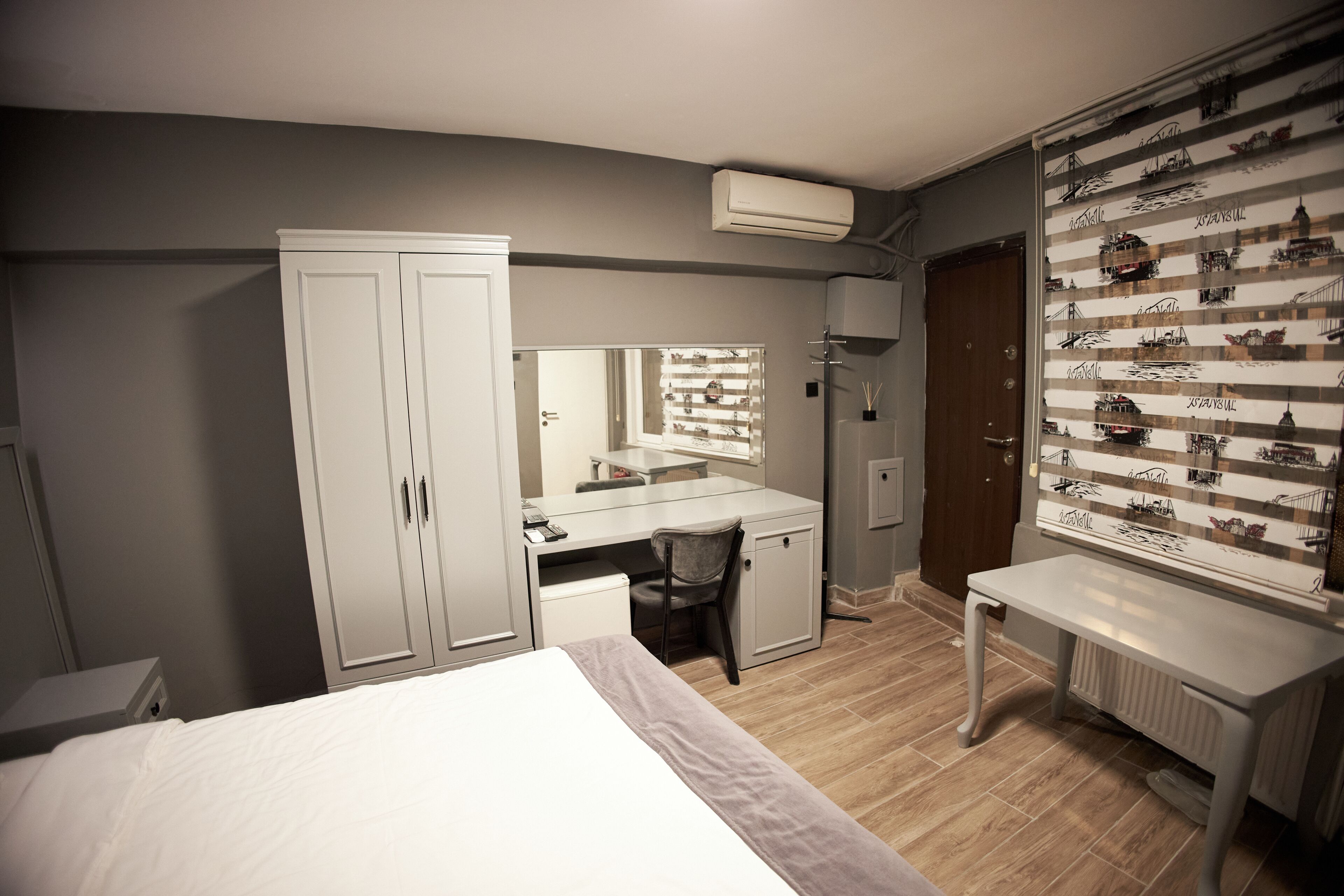 Une chambre d’hôtel comprenant un lit, un bureau avec une chaise, une armoire, un miroir et un mur décoré de tableaux.