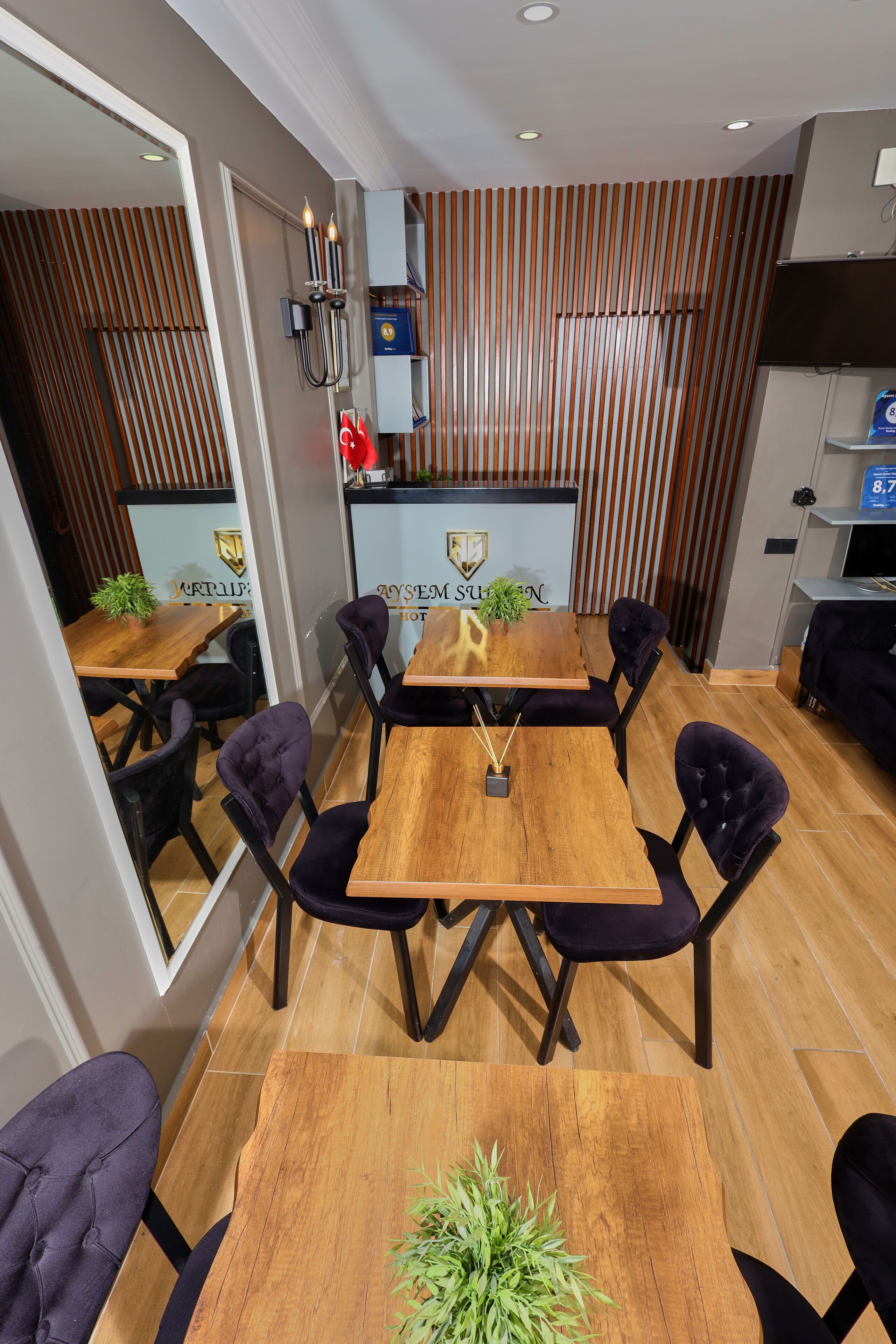 A modern dining area with a wooden table and black upholstered chairs, a potted plant, and a wall-mounted light fixture.