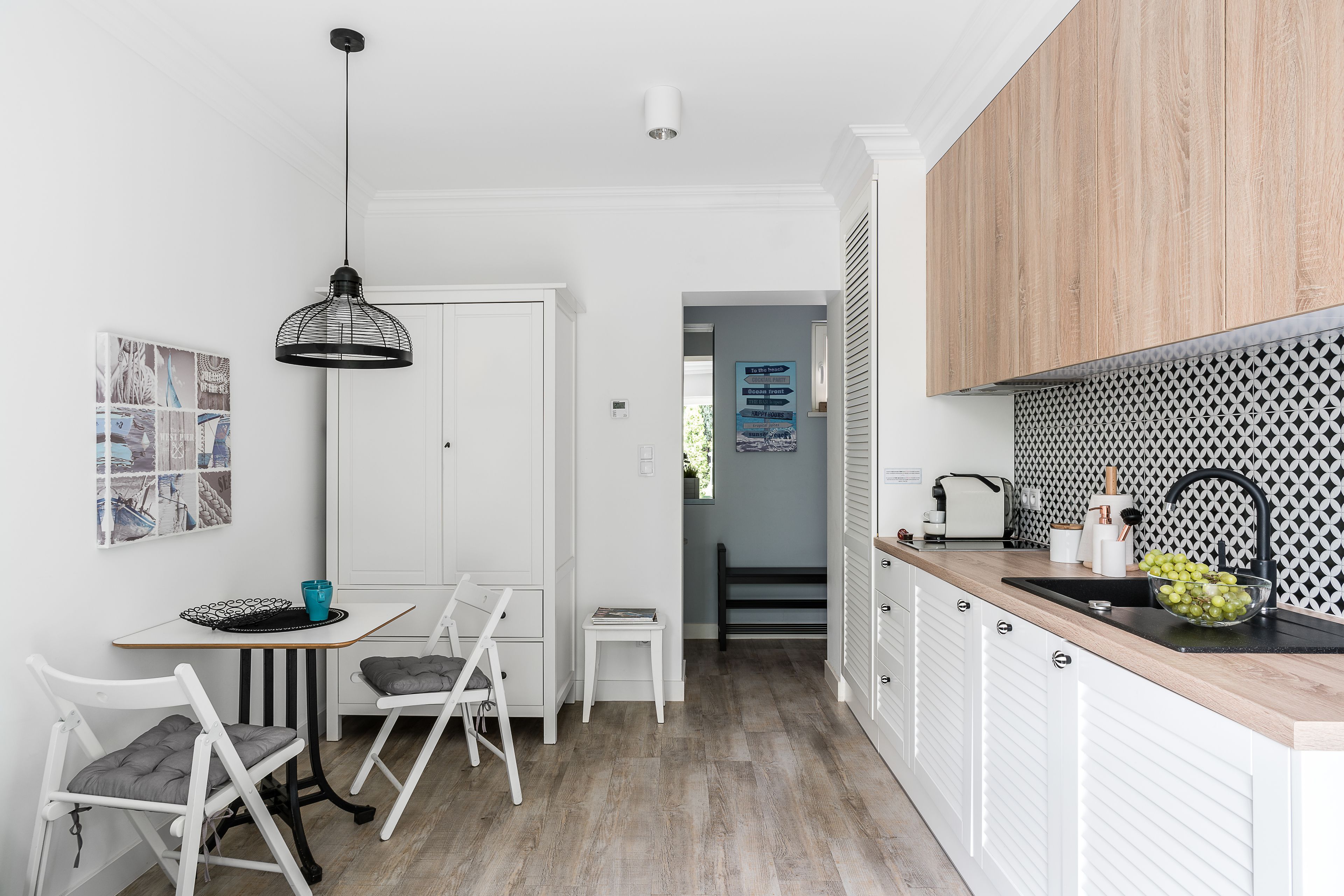 Eine moderne Küche mit weißen Schränken, einer Holz Arbeitsplatte und einer schwarz-weißen Spritzschutzwand. Es gibt einen Essbereich mit weißen Stühlen und einem Tisch, sowie eine hängende Leuchte.