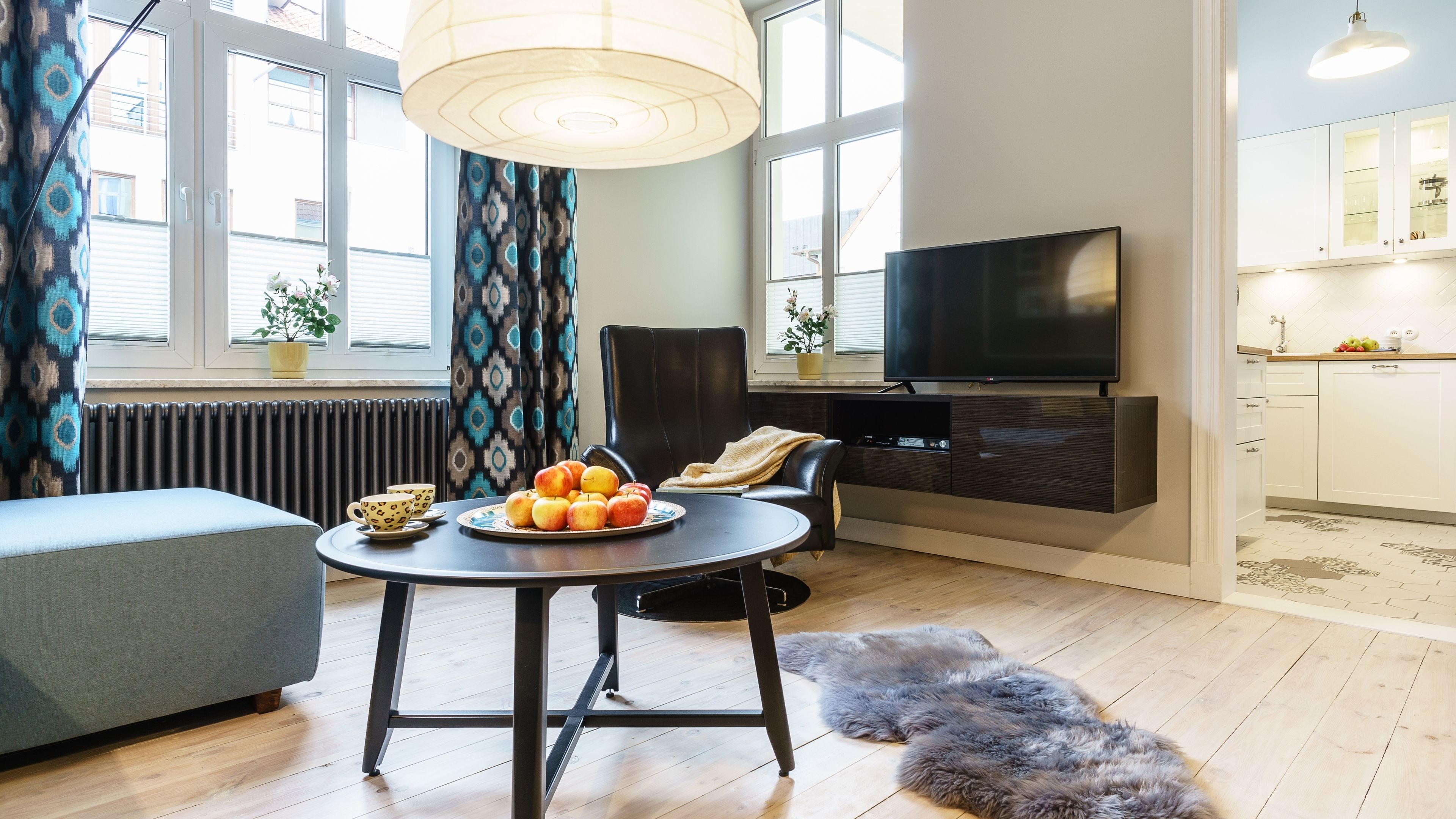 Una sala de estar moderna con un sofá, una mesa de comedor con fruta, un televisor y una zona de cocina con armarios.