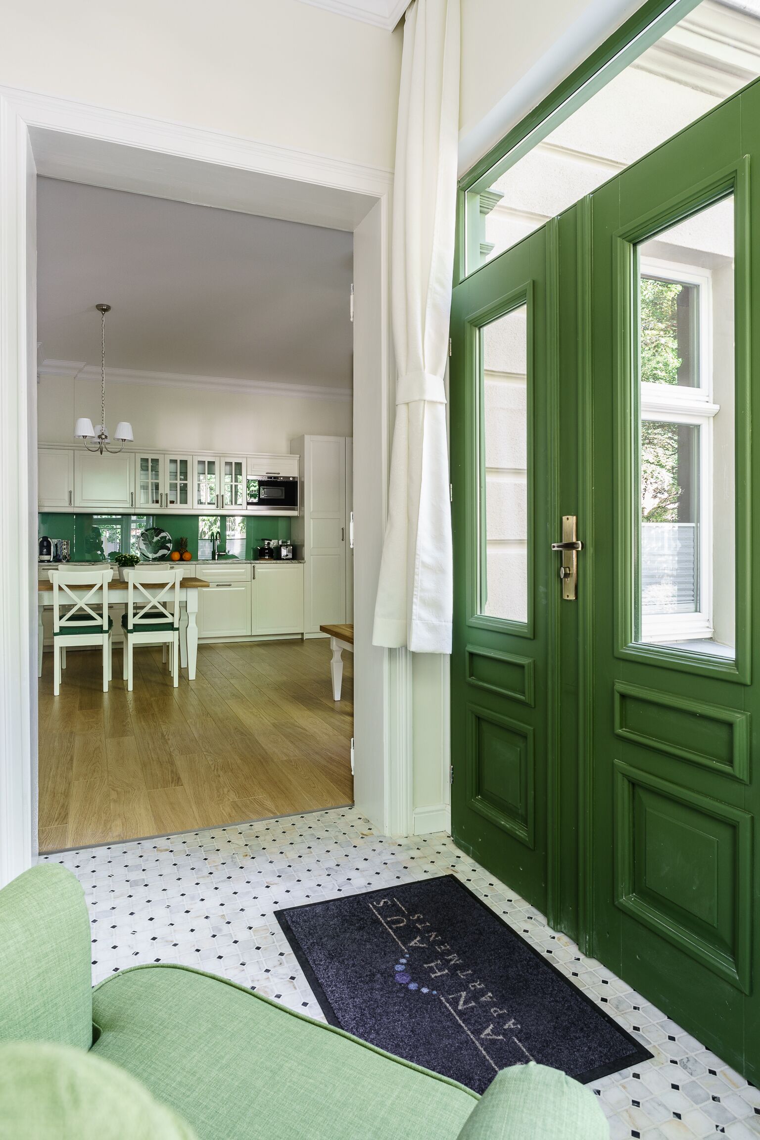 A modern kitchen with white cabinets, a green door, and a dining area with a bench and chairs.