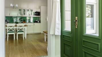 A modern kitchen with white cabinets, a green door, and a dining area with a bench and chairs.