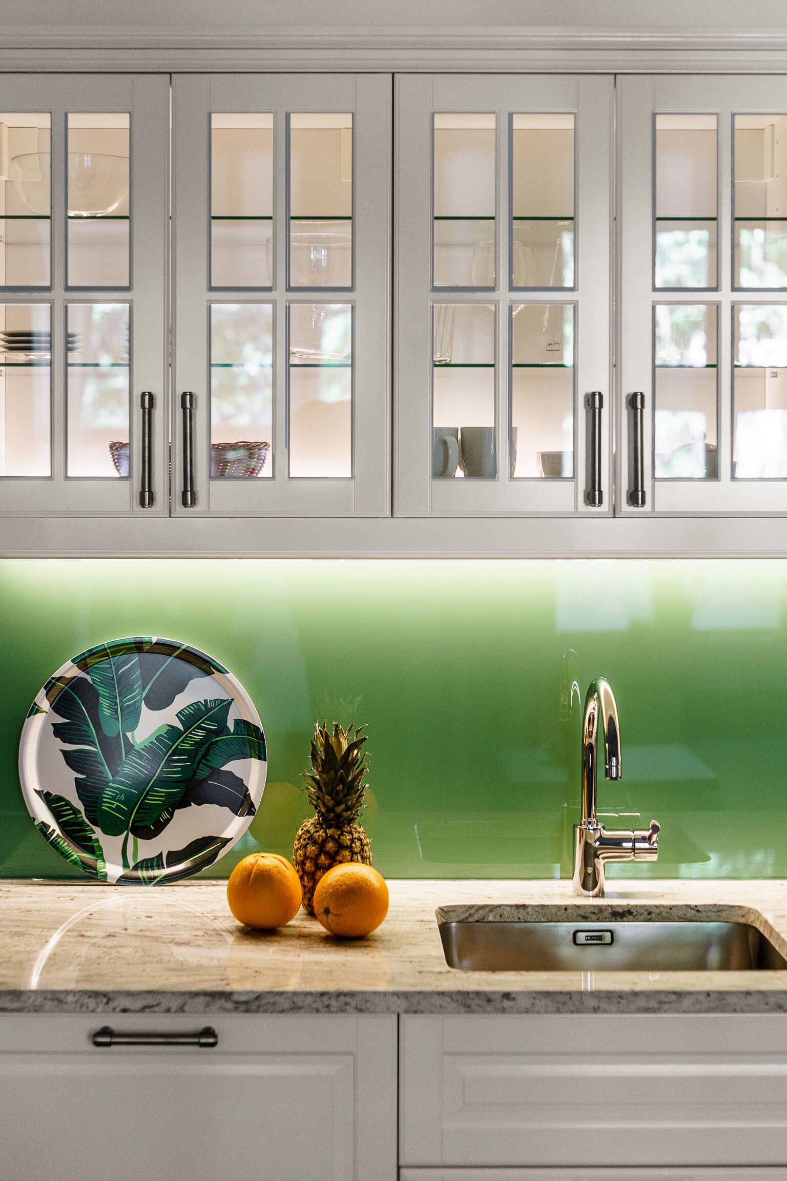A kitchen with white cabinets, a green backsplash, a stainless steel sink, and a decorative plate.