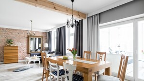 Un comedor con una mesa y sillas de madera, una araña y vistas al exterior a través de amplios ventanales.