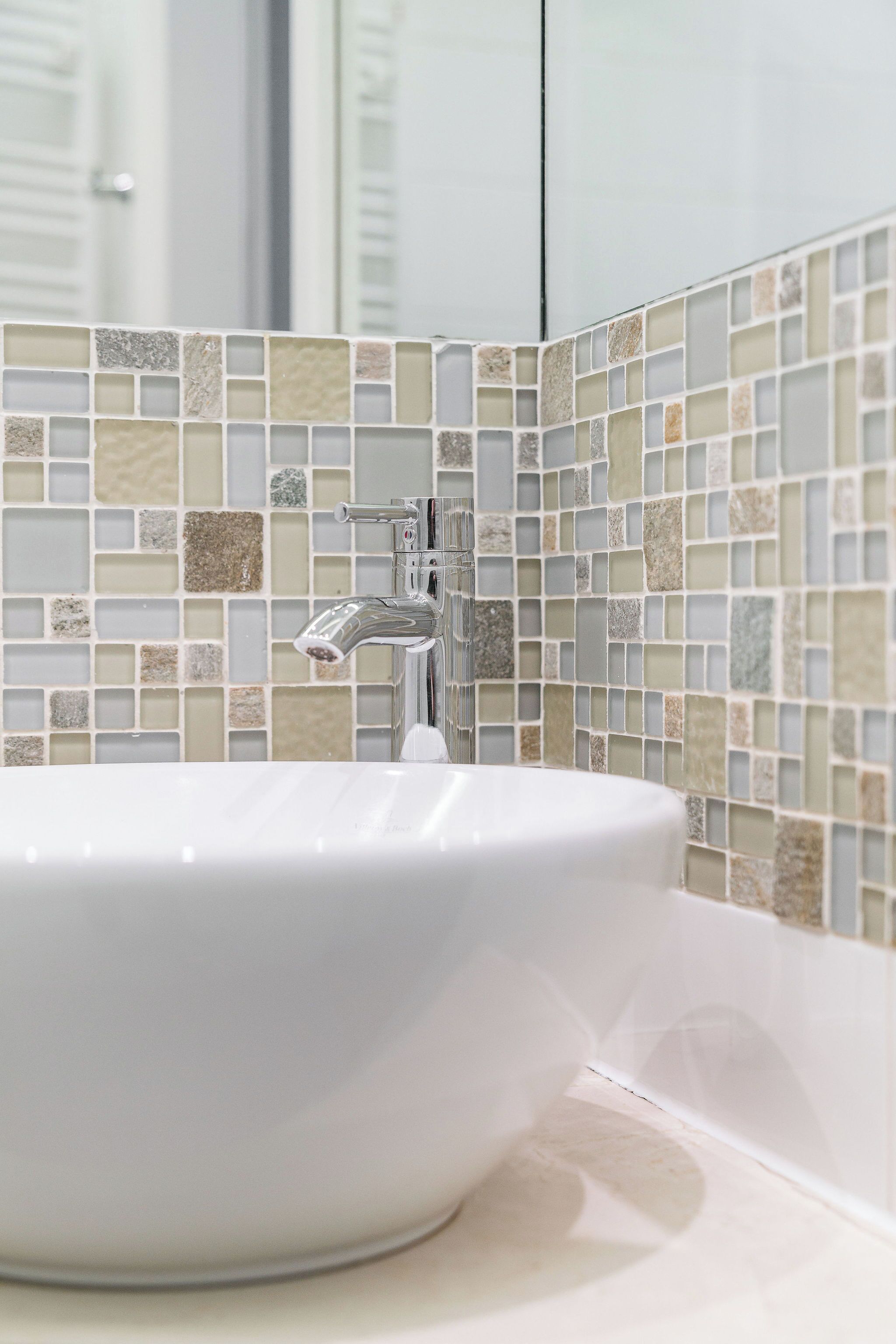 Un bagno con lavandino bianco, un rubinetto moderno e una parete di mosaico.