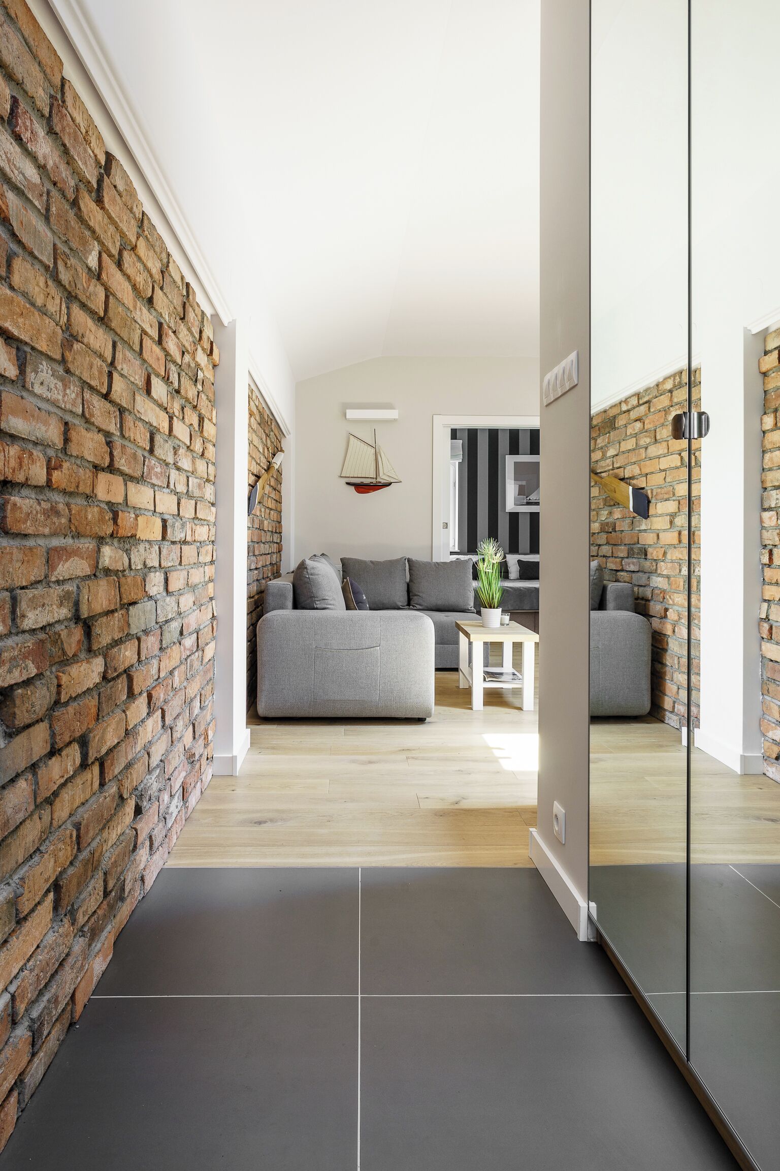 Una sala de estar moderna con pared de ladrillo, sofá gris y una pequeña mesa con una planta.