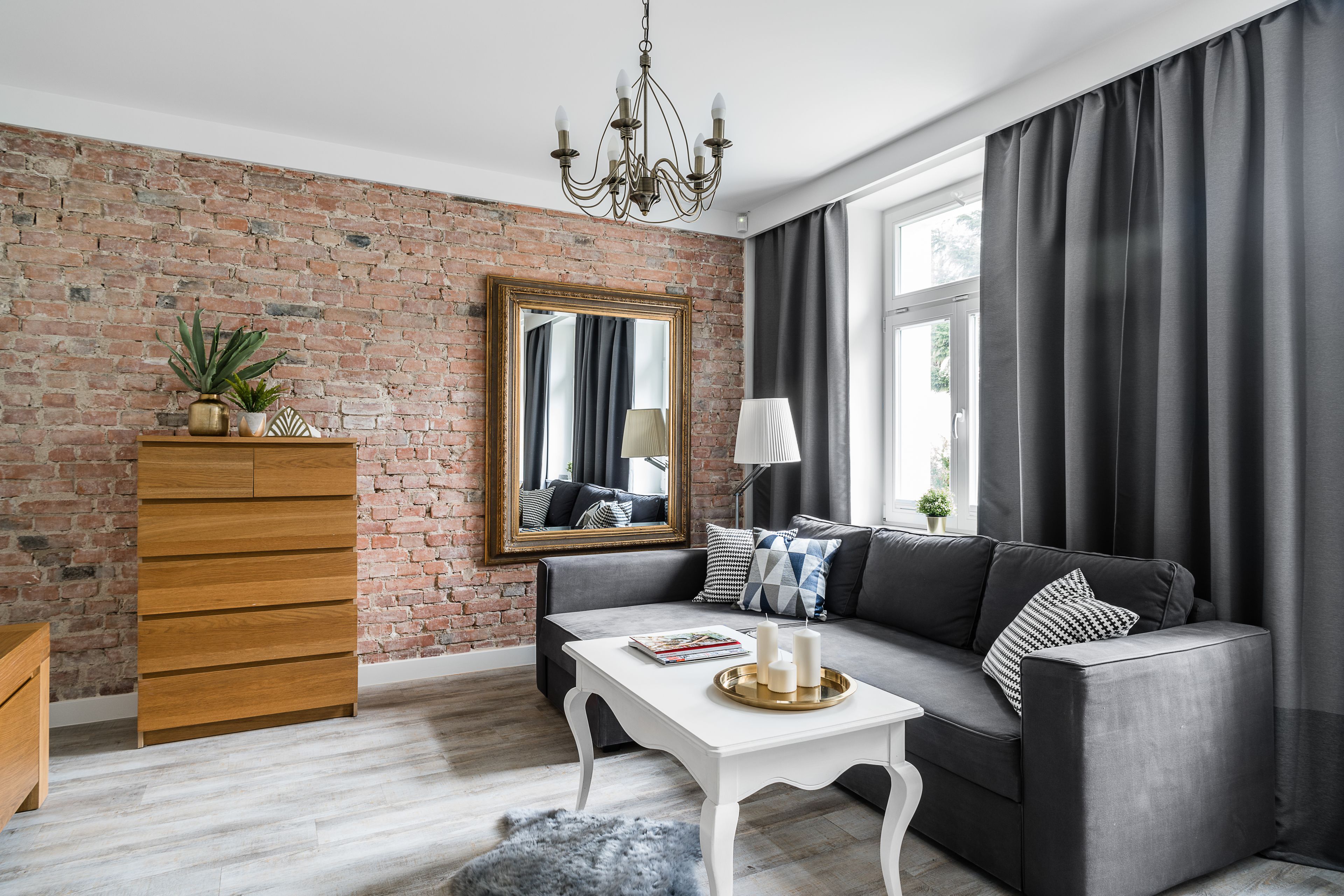 A living room with a brick wall, a sofa, a wooden cabinet, and a chandelier.