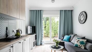 Eine moderne Küche mit Spüle, Herd und Fernseher. Ein Essbereich mit Tisch und Stühlen sowie eine Couch mit Kissen. Eine Uhr ist an der Wand.