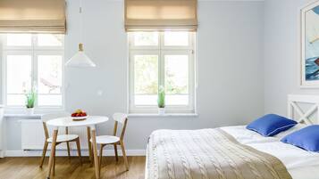 Una habitació amb un llit, una taula de dinar amb cadires i dues finestres amb persianes.