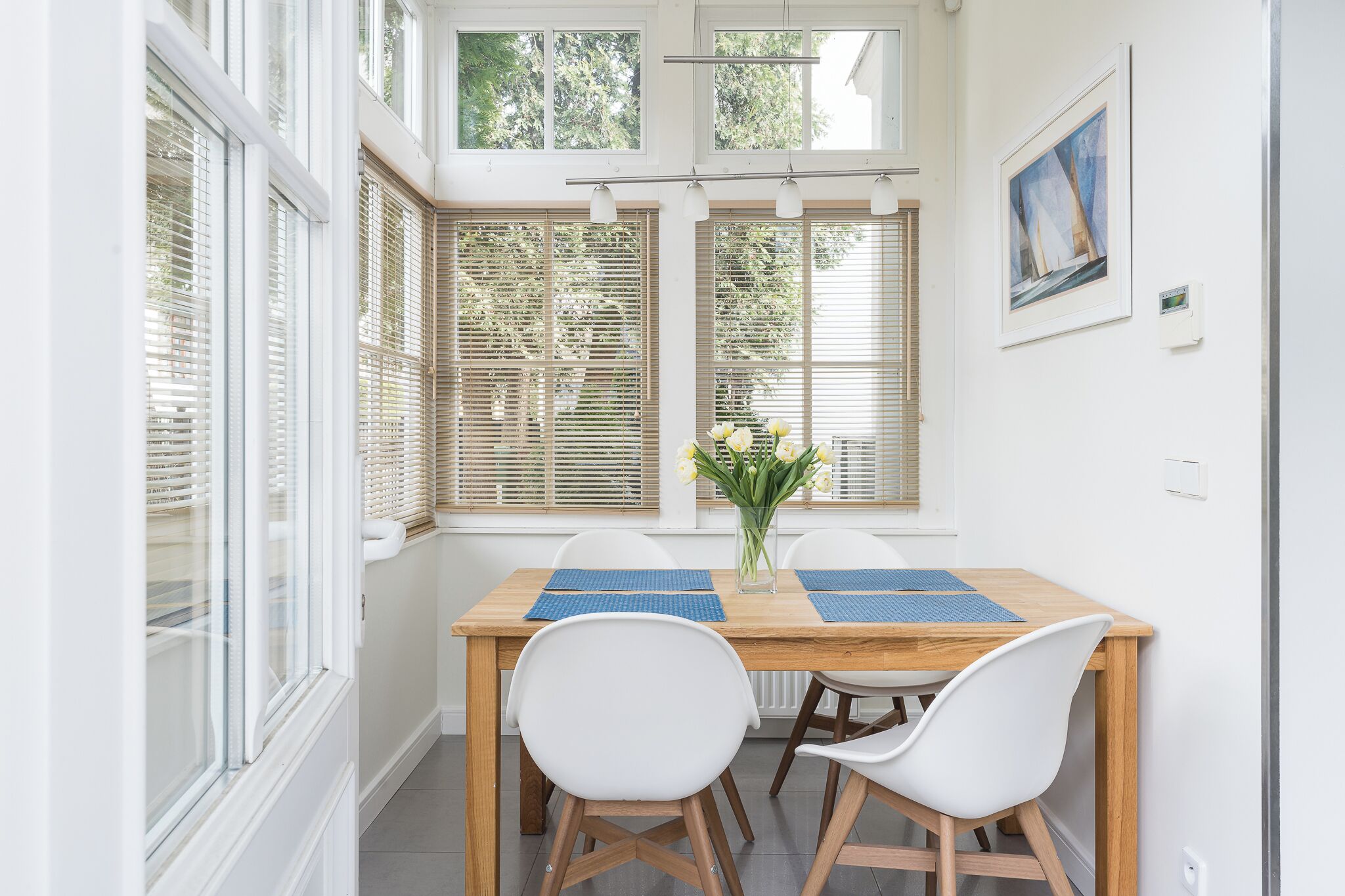 A dining area with a wooden table, white chairs, and a vase of flowers.