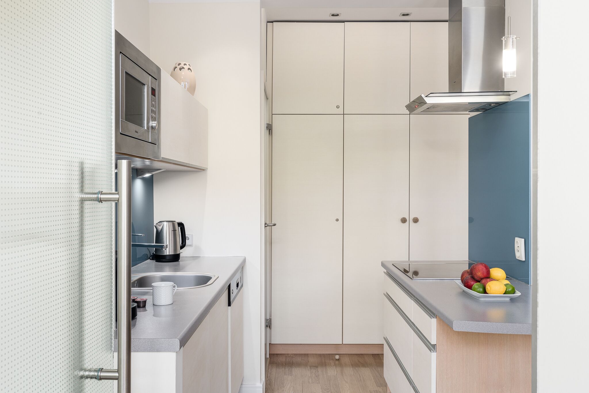 Una cucina compatta con forno a microonde, bollitore e una ciotola di frutta sul piano di lavoro.