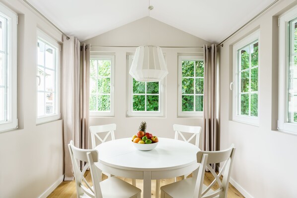 A dining room with a round table, white chairs, and a fruit bowl. - Sanhaus Apartments (Sopot)