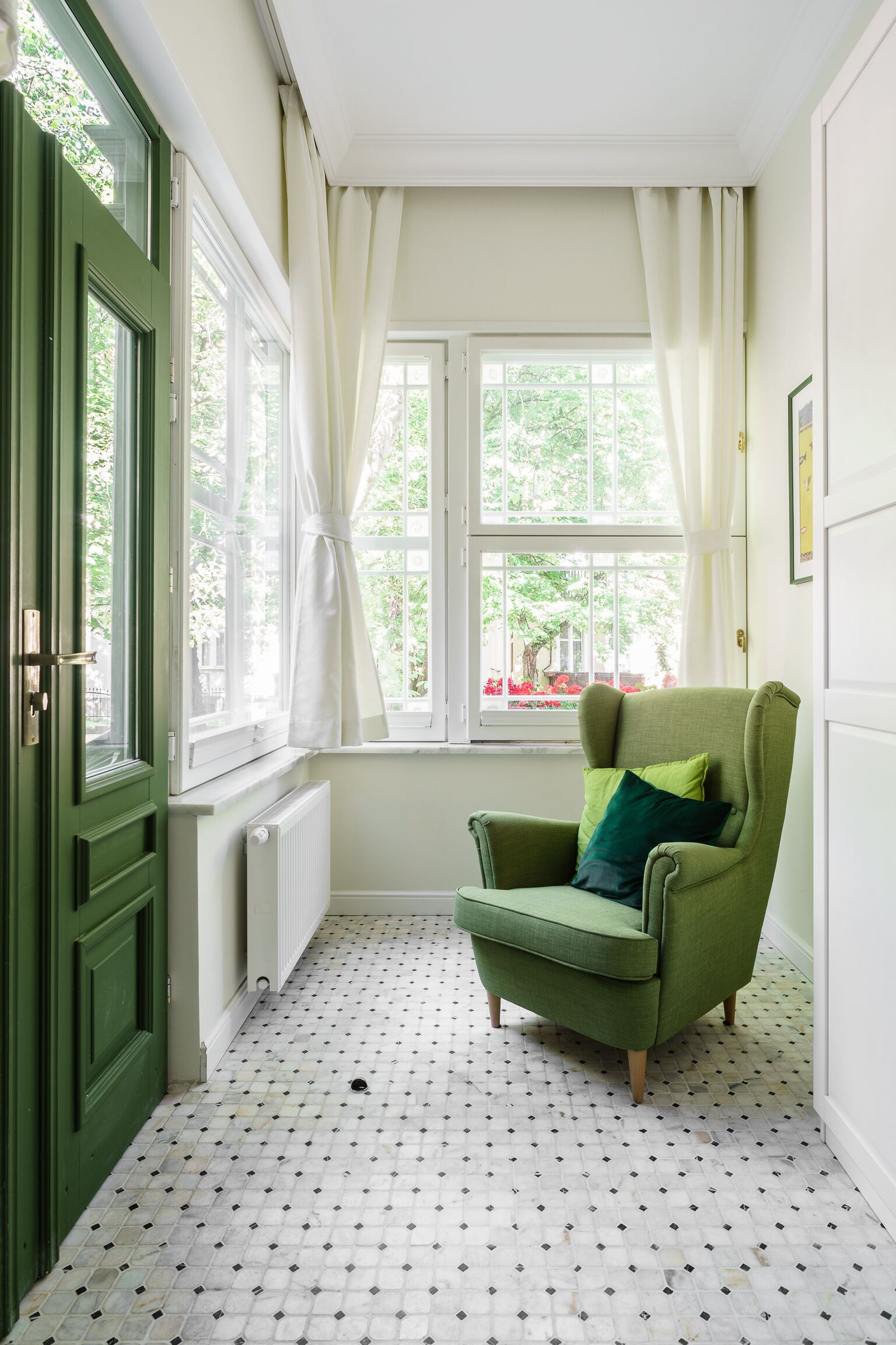 A room with a green armchair, a window with curtains, and a radiator.