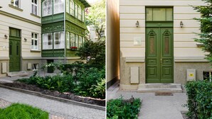 Un edificio con fachada verde, un conjunto de puertas dobles y un pequeño jardín con plantas.