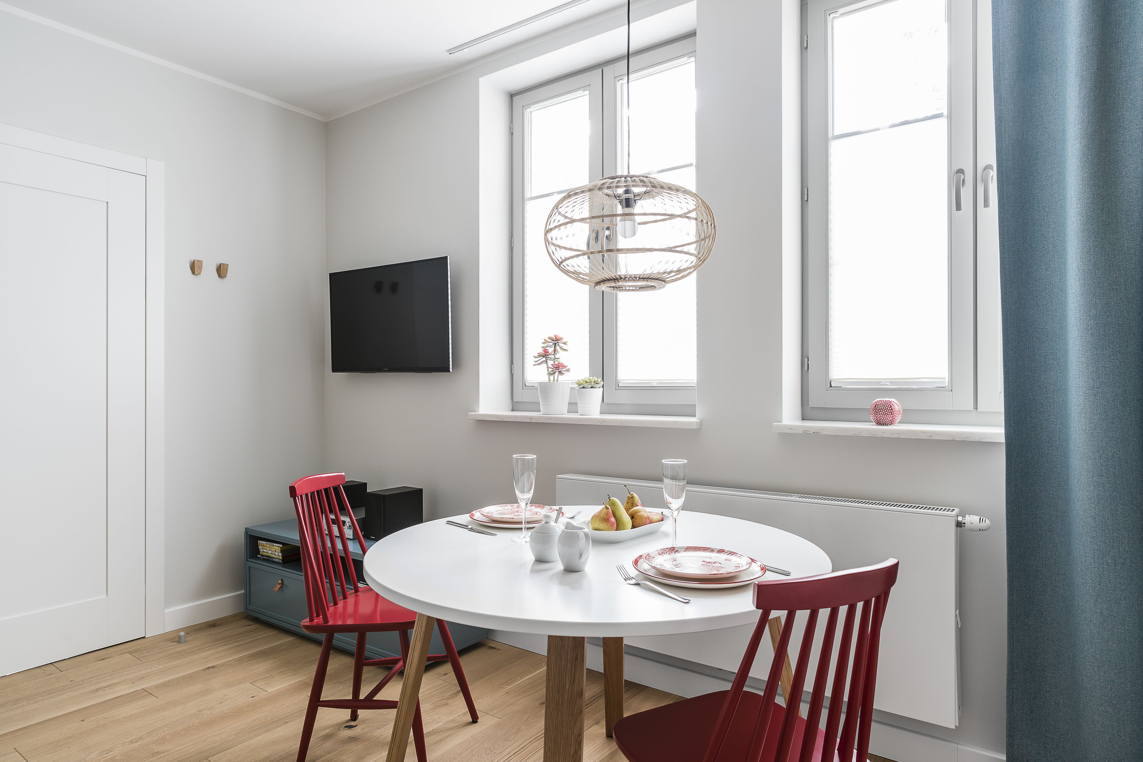 A dining area with a round white table, red chairs, and a fruit bowl.
