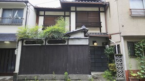A traditional Japanese house with a dark wooden gate, tiled roof, and a small garden area with plants. - Kyomachiya Shokokuji-an (Kyoto)