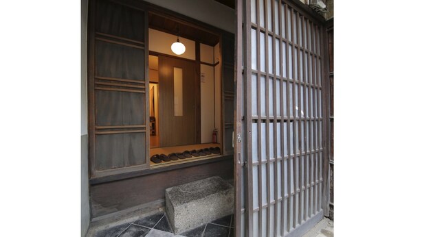 A traditional Japanese entrance with a sliding door, a small window with shoes displayed, and a stone step leading up to the door. - Kyomachiya Shokokuji-an (Kyoto)