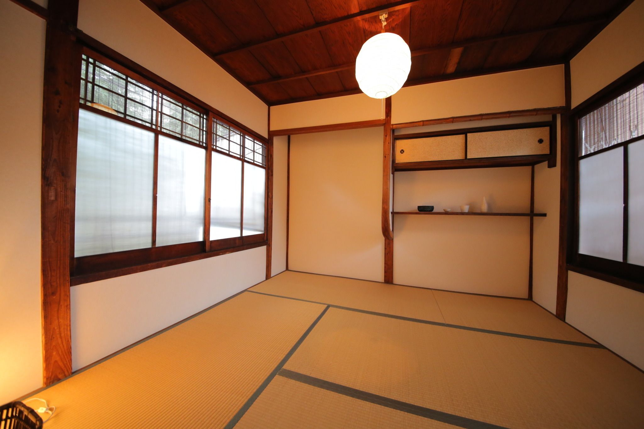A traditional Japanese room with tatami flooring, sliding doors, and a hanging light fixture.