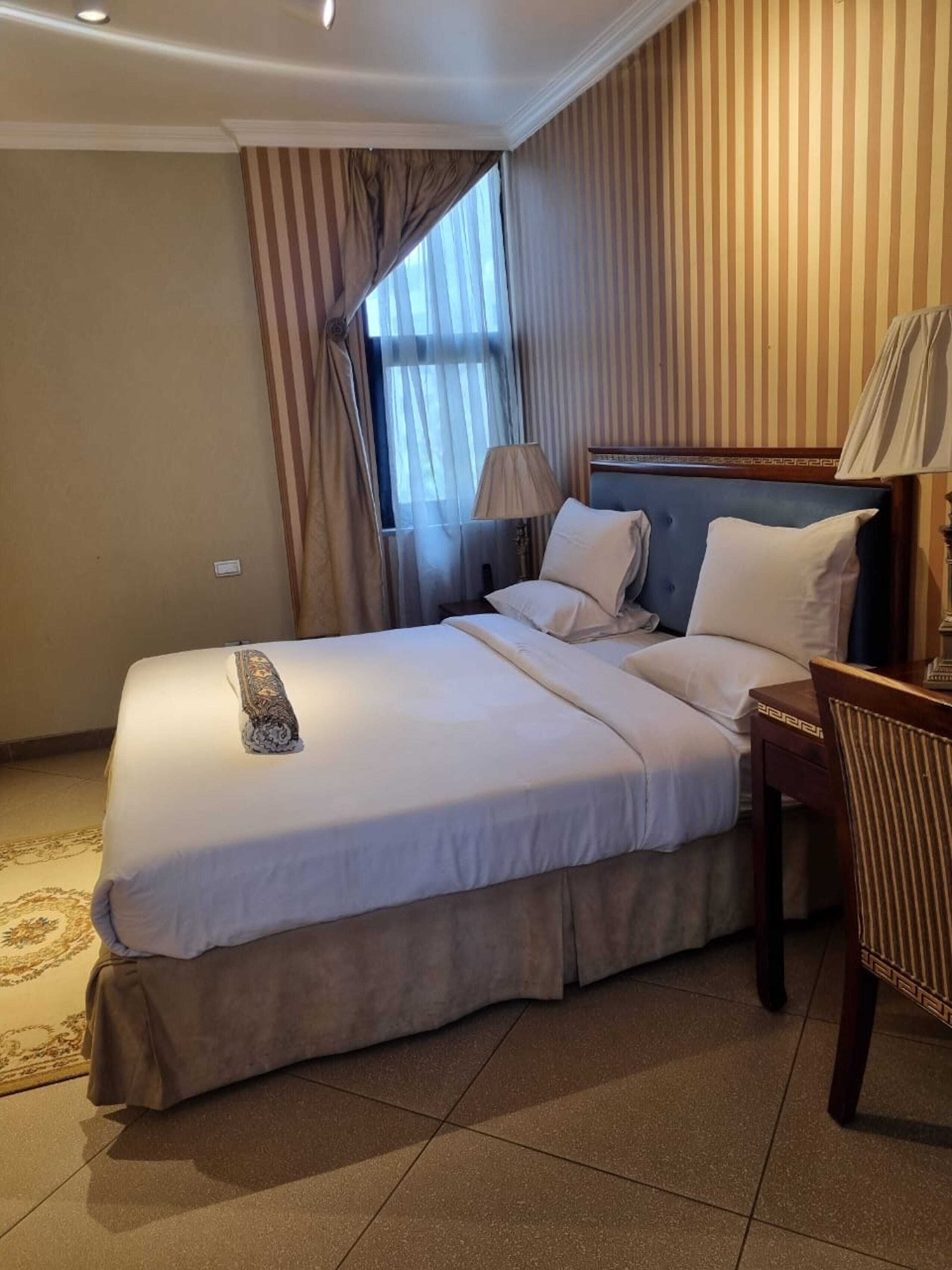 Hotellihuone, jossa on suuri sänky, yöpöytä, lamppu ja tuoli.