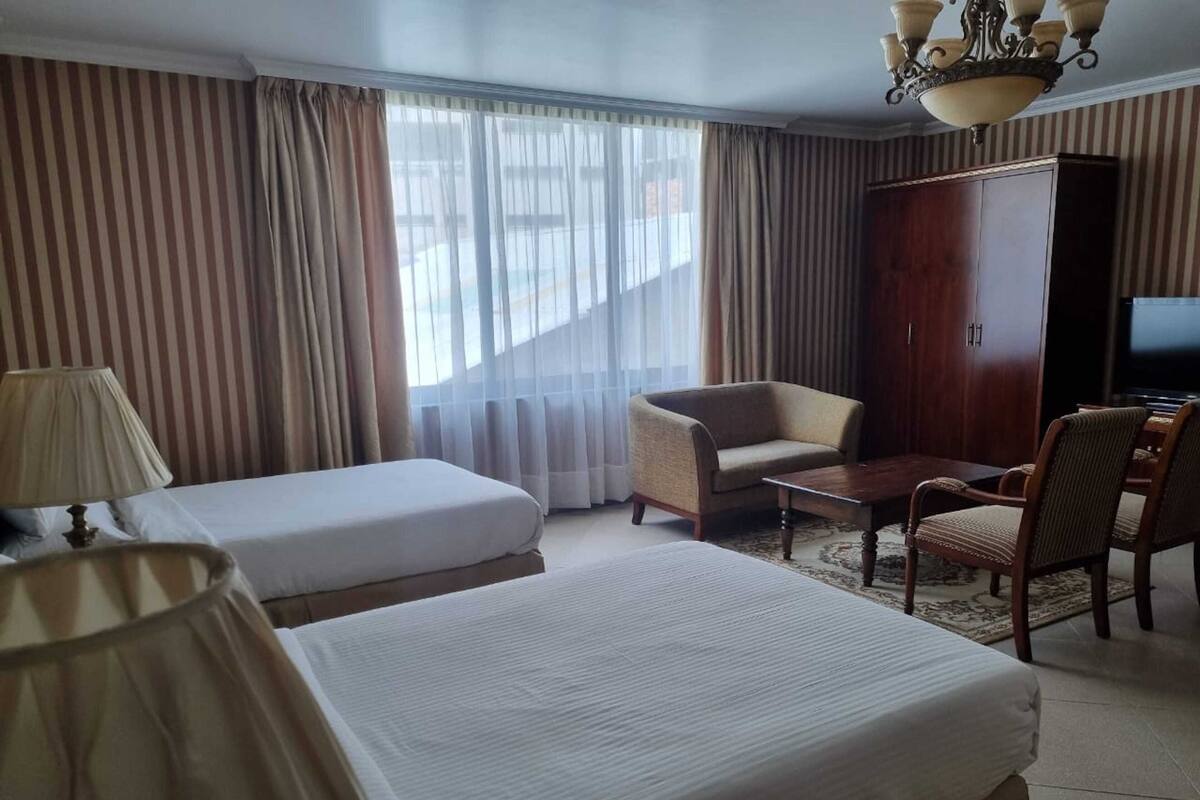 Quarto de hotel com duas camas, um sofá, uma TV e um guarda-roupa.