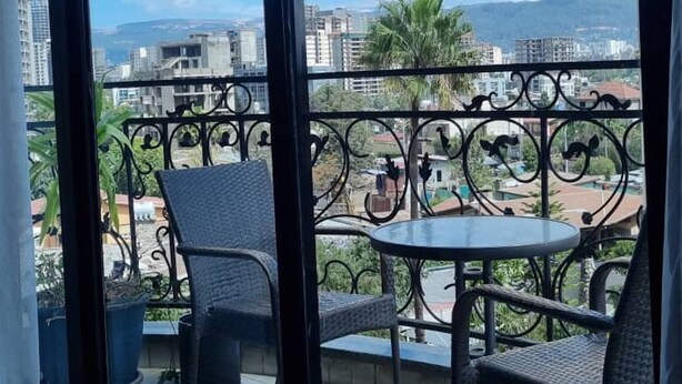 A balcony with two chairs and a table, overlooking a cityscape with buildings and palm trees. - The Residence Suite Hotel (Addis Ababa)