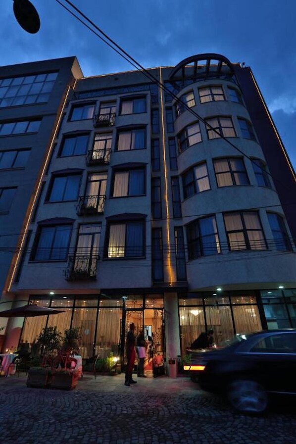 Ett hotell med flera våningar, en böjd fasad, stora fönster och en entré i markplan med uteservering.