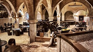 Un interior con arcos de piedra, mesas, sillas y barriles.
