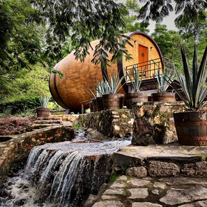 A rustic building with a wooden exterior, a stone pathway leading to a small waterfall, and potted plants around the area.