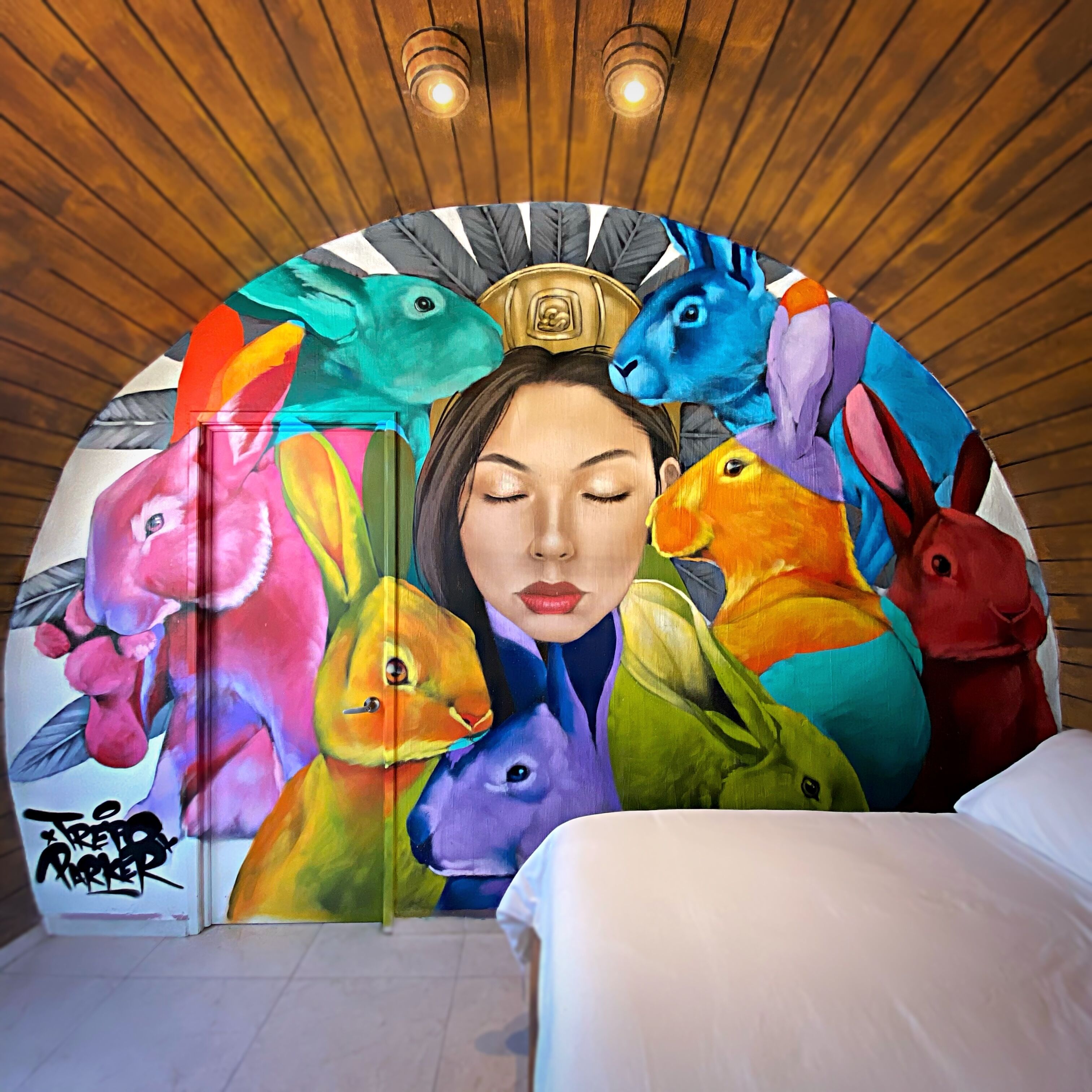 Una habitación con un mural de animales coloridos en la pared, una cama y paneles de techo de madera.