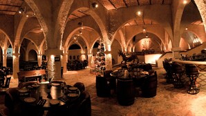 Un amplio salón con techos altos en arco y paredes de piedra, con varias mesas y sillas dispuestas para comer.
