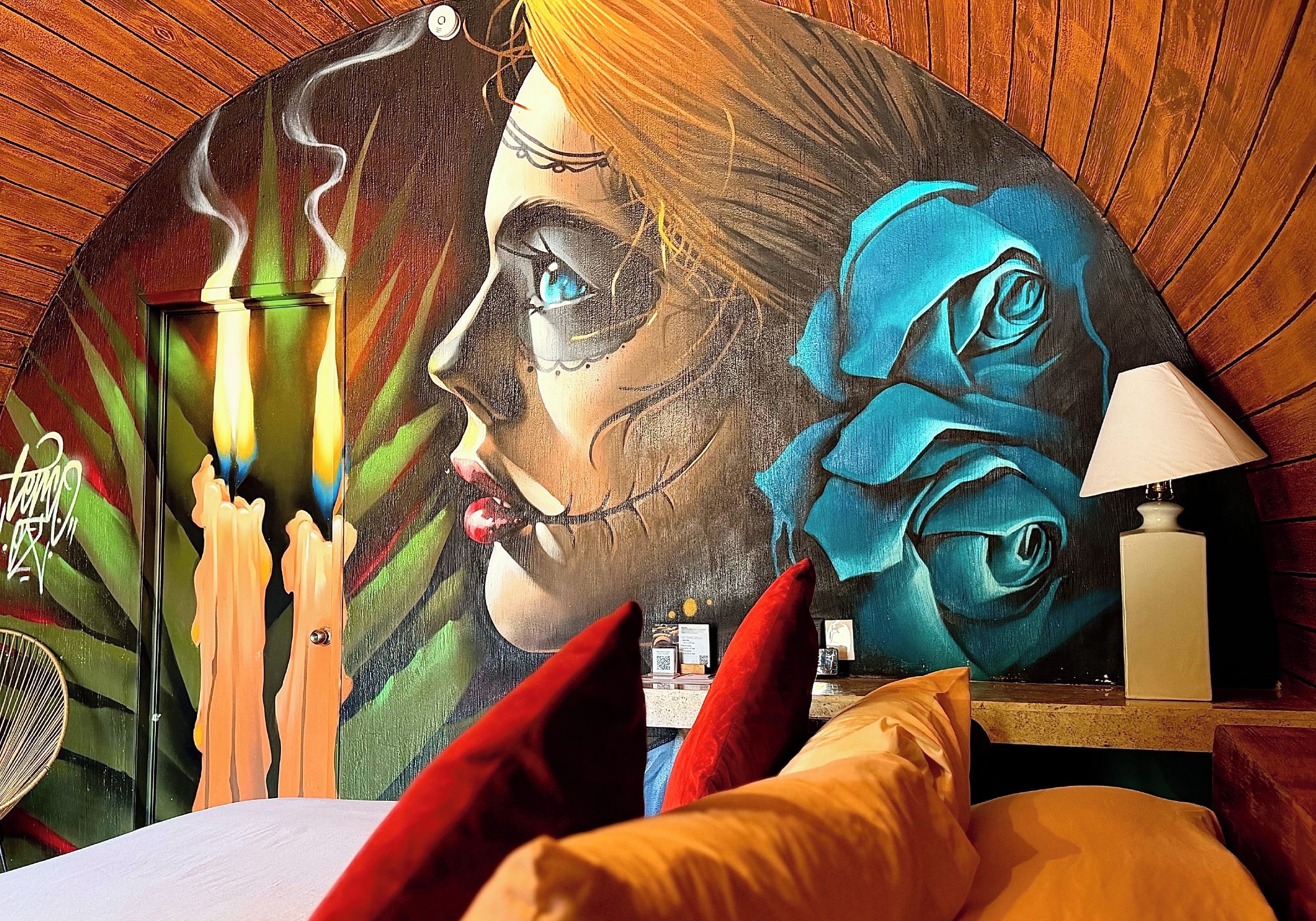 Una habitación con un mural, una cama, una mesita de noche y una lámpara.