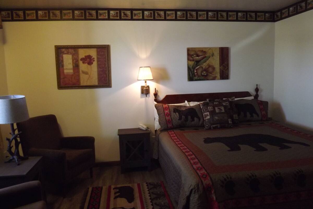 A hotel room with a bed, a chair, a lamp, and two wall-mounted paintings.