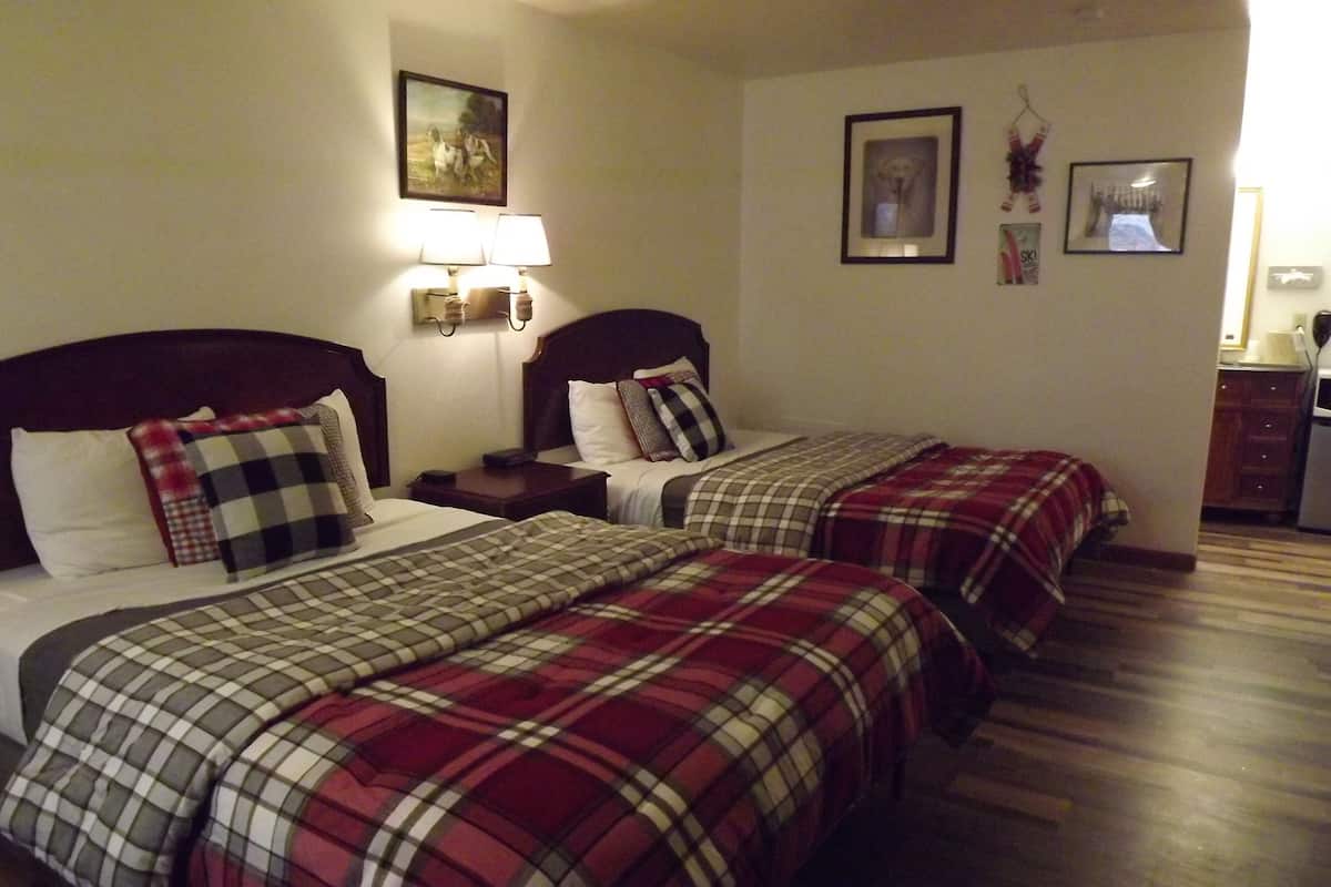 A hotel room with two beds, each with plaid bedding, a nightstand with a lamp, and a painting on the wall.