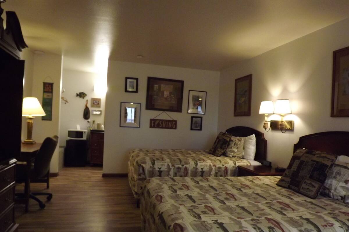 A hotel room with two beds, a desk, a chair, a microwave, and wall-mounted lamps.