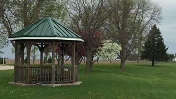 A gazebo with a green roof and wooden structure, surrounded by grass and trees.