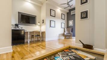 A modern living room with a wooden floor, a dining area with a table and chairs, a kitchen area with a black countertop, and a ceiling fan.