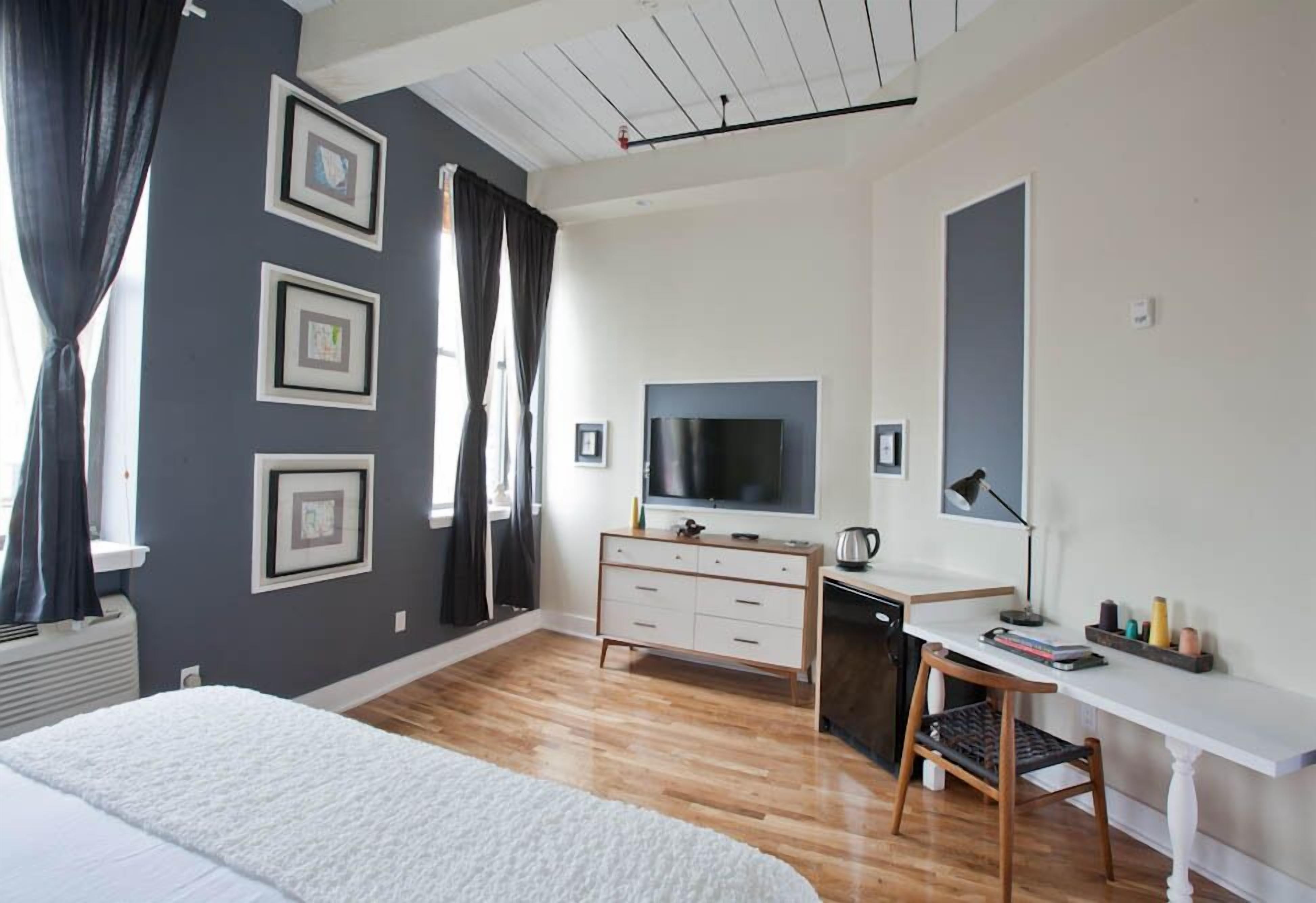 Une chambre d’hôtel moderne dotée d’un grand lit, d’un bureau avec un ordinateur, d’une télévision à écran plat et d’une fenêtre avec des rideaux.