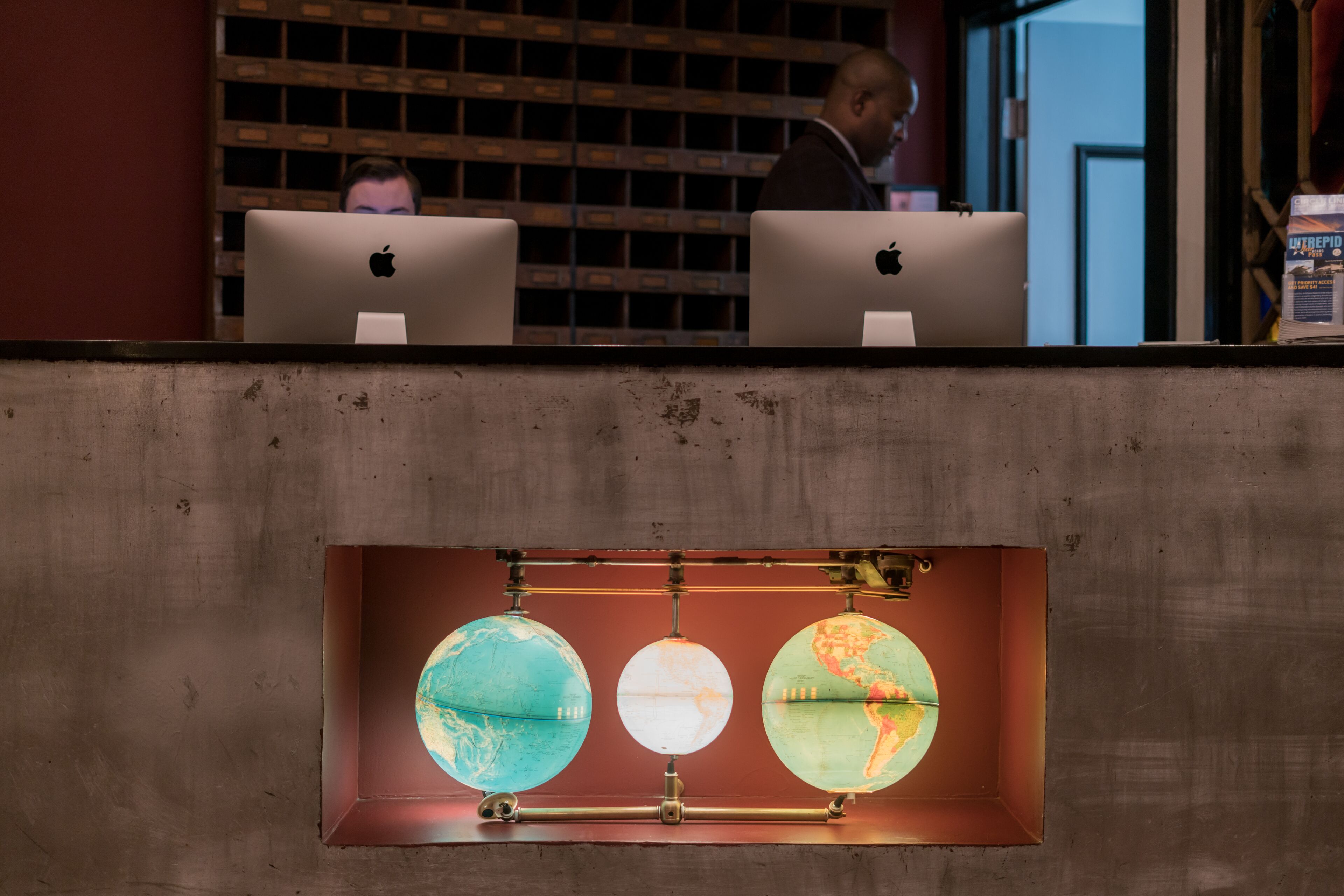 A desk with two laptops and three illuminated globes in a recessed shelf.