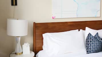 Una cama bien tendida con almohadas blancas y estampadas, una lámpara de noche y un mapa mural.