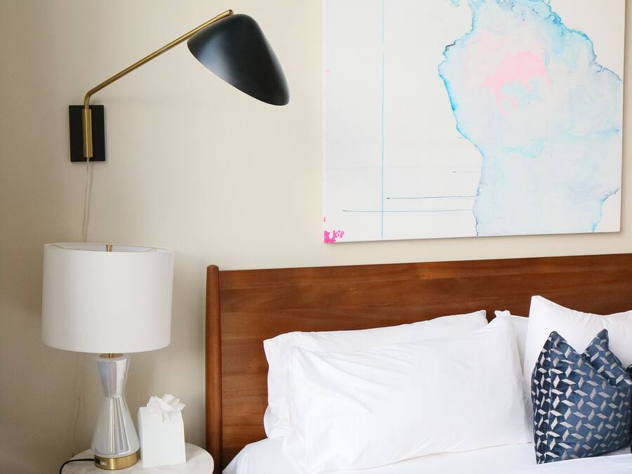 Una cama bien tendida con almohadas blancas y estampadas, una lámpara de noche y un mapa mural.