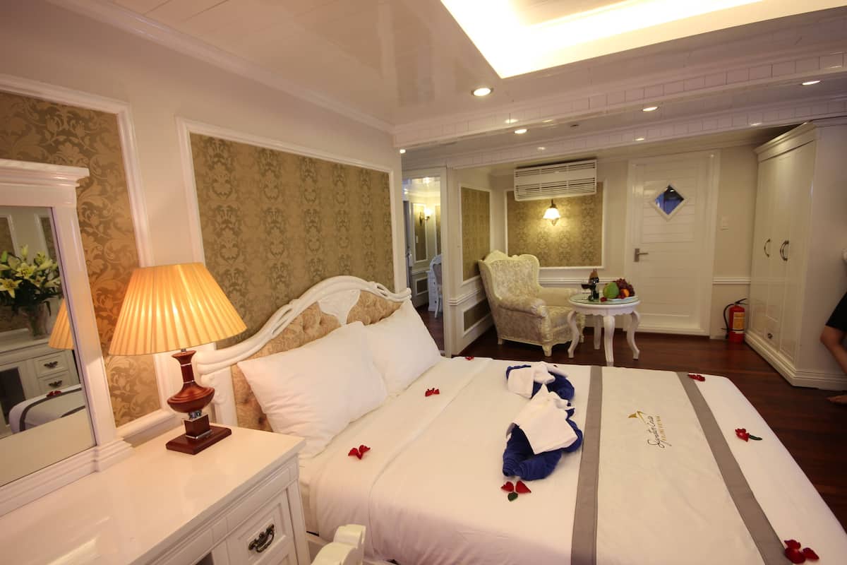 Quarto de hotel com cama, mesa de cabeceira com abajur, cadeira, mesinha com um vaso e guarda-roupa.