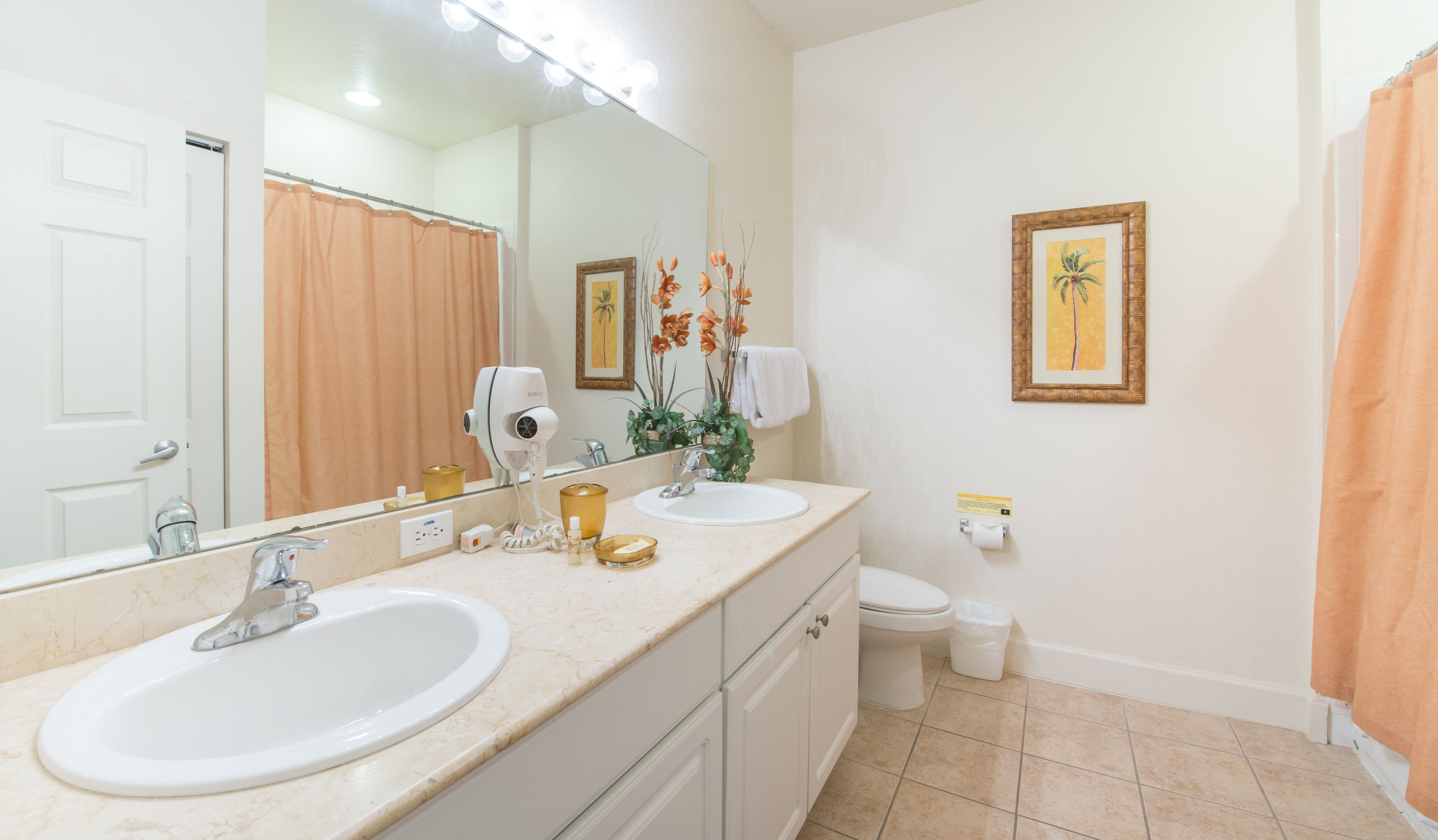 A bathroom with two sinks, a toilet, a shower curtain, a large mirror, and decorative plants.