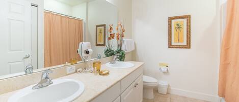 A bathroom with two sinks, a toilet, a shower curtain, a large mirror, and decorative plants.
