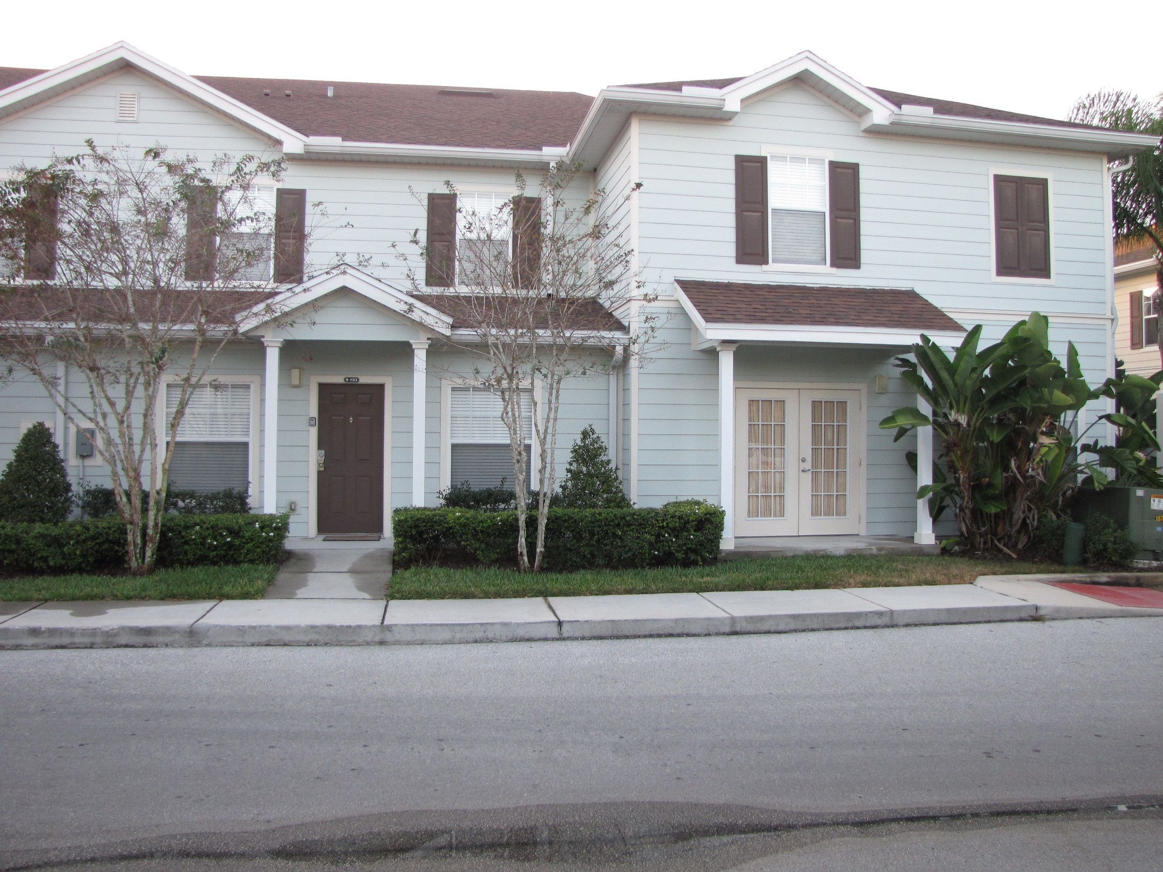 A row of two-story townhouses with front porches, a garage, and a small front yard with a tree and shrubbery.